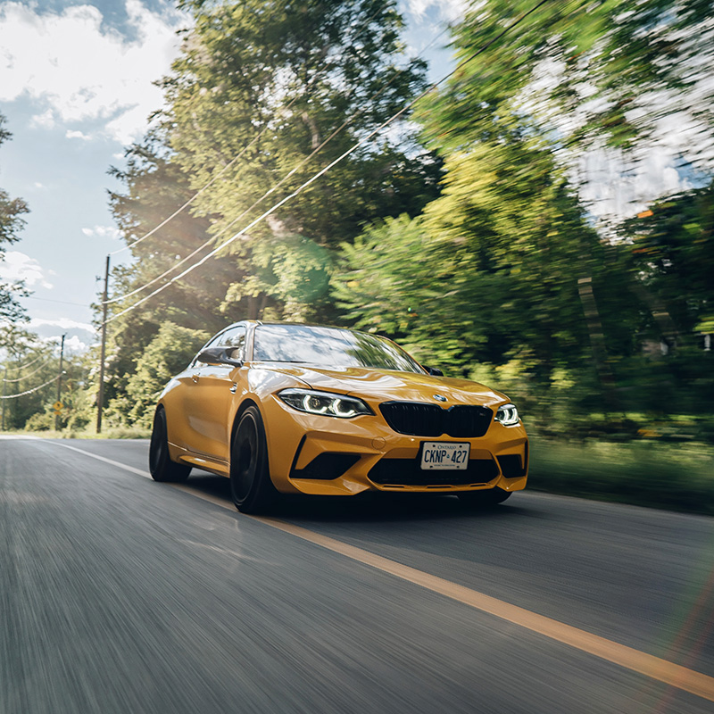 A yellow BMW driving on a road