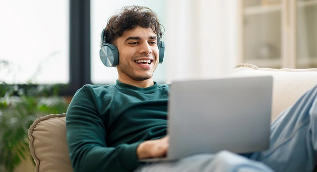 A man wearing headphones and looking at his laptop on the couch